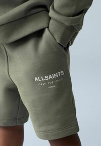 Oliivinvihreät shortsit pehmeästä kankaasta, joissa on resorivyötärö ja sivutasku. "ALLSAINTS"-logo valkoisella tekstillä lahkeessa.