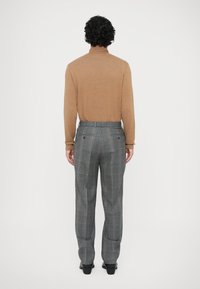 Pull en col roulé marron associé à un pantalon à carreaux gris avec des accents bleus et orange. La coupe est ajustée avec une texture lisse.