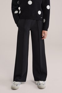 Fekete bő szárú nadrág redőkkel, sima anyagból, világosszürke és ezüst tornacipővel párosítva. Az öltözéket pöttyös pulóver egészíti ki.