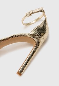Goldfarbene High Heels mit einer strukturierten Schuppenleder-Oberfläche, einem Knöchelriemen mit Schnalle und einem spitzen Zehendesign.