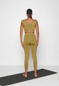 Olivgrünes Sportset mit einem cropped, ausgeschnittenen Oberteil und hoch taillierten Leggings. Glatter, elastischer Stoff mit subtilen Nahtdetails.