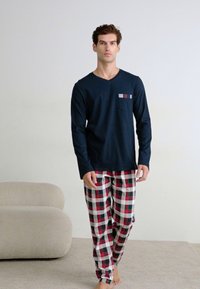 Maglietta a maniche lunghe blu navy con taschino sul petto; pantaloni da pigiama a scacchi in rosso, verde e bianco; tessuto morbido; vestibilità rilassata.