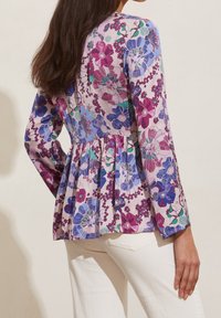 Blommig blusa med peplumdesign, tillverkad av lättviktsmaterial i nyanser av lila, rosa och blått, med lång ärm och rund halsringning.