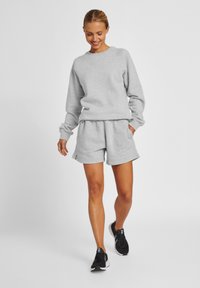 Grauer Sweatshirt mit gerippten Bündchen, kombiniert mit passenden grauen Shorts. Das Outfit hat eine lockere Passform und seitliche Taschen. Getragen mit schwarzen Turnschuhen.