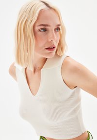 Top a coste, senza maniche, in off-white con scollatura a V profonda e colletto a contrasto. Tessuto a maglia leggero. Forma aderente.
