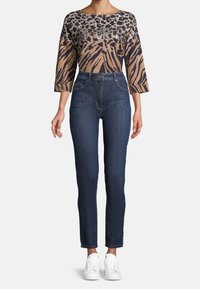 Brun och svart mönstrad topp med trekvartsärmar, kombinerad med figursydda mörkblå jeans och vita sneakers.