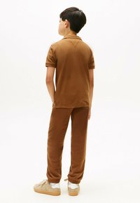 Brun bomulds polo skjorte og matchende bukser med en afslappet pasform. Skjorten har en krave; bukserne har elastiske manchetter og lommer. Beige sneakers.