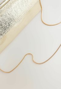 Pochette métallique dorée avec une longue bandoulière en chaîne dorée sur une surface claire.