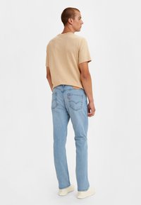 Camiseta de algodón beige de manga corta, combinada con jeans de denim azul claro. Los jeans cuentan con un parche de logo en la parte trasera y dos bolsillos en la parte posterior.