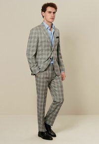 Traje de cuadros gris con chaqueta de dos botones y pantalones de frente plano. Presenta una camisa de color azul claro debajo y zapatos negros. Textura y patrón sutiles.