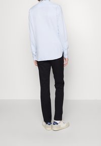 Světle modrá košile s dlouhým rukávem a knoflíkovými manžetami, spárovaná s černými úzkými kalhotami a bílými teniskami s modrými akcenty na patě.