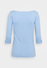 Light blue 3/4 sleeve top with a wide neckline, featuring rolled cuffs with button accents and smooth, soft fabric texture.