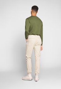 Långärmad olivgrön skjorta, beige cargobyxor och beige högskor. Skjortan är åtsittande; byxorna har sidofickor och smalnade ben.