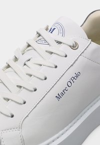 Αθλητικό παπούτσι από λευκό δέρμα με λευκά κορδόνια, μεταλλικά κορδόνια, λογότυπο Marc O’Polo στο πλάι και κυκλικό λογότυπο στη γλώσσα.