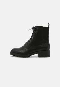 Black ankle boot with textured leather upper, lace closure, and silver eyelets. Chunky rubber sole with a block heel. Back pull tab.