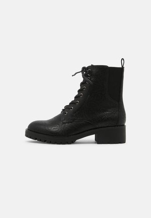 Musta nilkkuri, jossa on teksturoitu nahkapinta, nauhakiristys ja hopeiset rei'itykset. Paksu kumipohja ja lohkarekorko. Takana vetonauha.