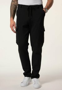 Zwarte cargo joggers met elastische tailleband, verstelbaar trekkoord en twee zijzakken. Gemaakt van zachte stof, gecombineerd met witte sneakers.