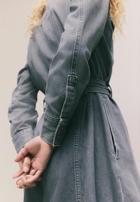 Graham Denimkleid mit langen Ärmeln, taillierter Taille und seitlichen Taschen. Verfügt über einen knöpfbaren Manschette und ein entspanntes, fließendes Design.