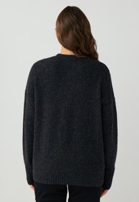 Ciemnoszary, oversize sweter z teksturowanego materiału wełnianego, z prążkowanymi mankietami i okrągłym dekoltem. Widoczny luźny krój i miękka powierzchnia.
