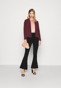 Bordeaux jasje met een getailleerde pasvorm, lichtroze gathered top, zwarte flared broek en een blush clutch. Zwarte open teen hakken.