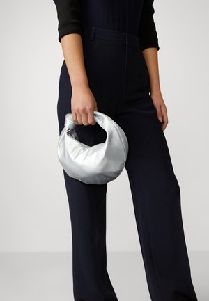 Srebrna torba syntetyczna z supełkowanym uchwytem, o miękkiej, gładkiej fakturze. Noszona z ciemnymi, szerokimi spodniami.