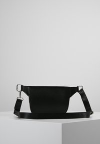 Bolso de cuero negro con textura suave, forma rectangular y correa ajustable. Cuenta con detalles de herrajes metálicos y un diseño minimalista.
