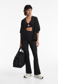 Zwarte sportoutfit met een cropped zip-up hoodie, een bralette met een keyhole, hoge taille leggings en witte sneakers. Zwarte sporttas.