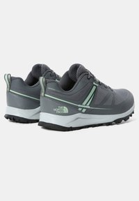 Grå idrottsskor i nät- och syntetmaterial. Har en strukturerad yta, svart gummisula och subtila gröna detaljer.