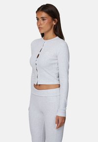Light gray cropped long-sleeve top with a round neck, buttoned front, and ribbed texture. Paired with matching light gray leggings.