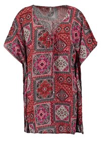 Tunique rouge et rose à motifs avec une coupe décontractée, décolleté en V et manches courtes. Présente un mélange de designs géométriques et floraux. Tissu léger.