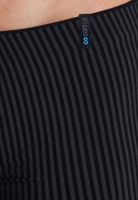 Tissu noir rayé avec une texture douce. Présente une étiquette portant la mention "LONGUE DURÉE DOUCE" en bleu. Le design comprend de fines rayures verticales.