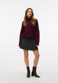 Bordeaux oversized trui met geribbelde textuur, gecombineerd met een grijze plooienrok. Zwarte leren enkellaarsjes maken de outfit compleet.