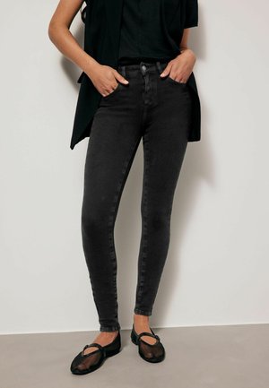 Černé skinny džíny z denimu s vysokým pasem, vybavené předními kapsami a minimalistic designem, v kombinaci s černými plochými botami.