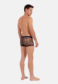 Herren-Badehosen mit tailliertem Design, schwarzem Hintergrund und buntem tropischem Blumenmuster. Elastischer Bund, kurze Länge, glatte Textur.
