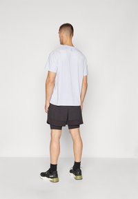 Camiseta de manga corta de color azul claro con cuello redondo, combinada con pantalones cortos deportivos negros. El conjunto presenta un ajuste relajado y un diseño minimalista.