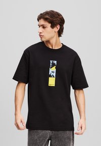 Svart bomulls t-skjorte med et sentralt grafisk design i blått og gult, rektangulær form, med korte ermer og rund hals.