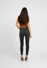 Vaqueros pitillo negros de talle alto, con bolsillos traseros y una textura lisa y elástica. Combinados con tacones de tiras negras.