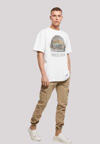 Camiseta blanca de algodón con un gráfico de un personaje con casco, combinada con pantalones cargo beiges y zapatillas blancas.