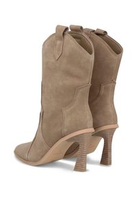 Botas de tobillo de ante beige con punta afilada, diseño de corte curvado y tacón alto con finas franjas. En la parte posterior cuentan con pequeñas pestañas de agarre.