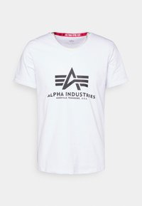 Bílá bavlněná tričko s výstřihem do V a krátkými rukávy. Obsahuje černé grafické logo a text "ALPHA INDUSTRIES KNOXVILLE, TENNESSEE, U.S.A."
