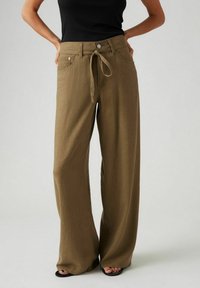 Pantalones de pierna ancha en color verde oliva, elaborados con una tela suave. Cuentan con un lazo frontal, bolsillos y un corte relajado. Textura suave con detalles mínimos.