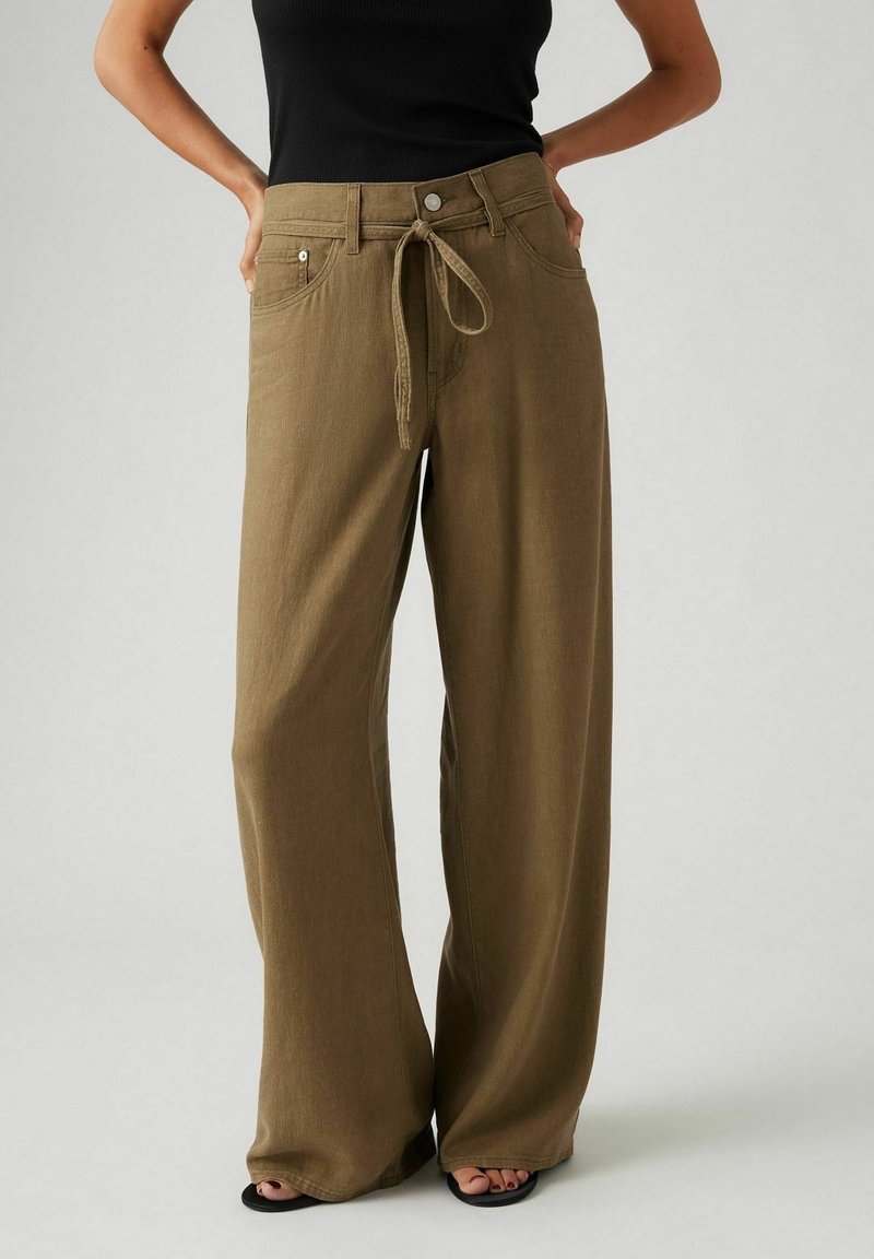 Pantalones de pierna ancha en color verde oliva, elaborados con una tela suave. Cuentan con un lazo frontal, bolsillos y un corte relajado. Textura suave con detalles mínimos.