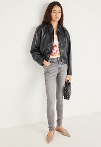 Czarna kurtka ze skóry ekologicznej, różowo-żółta bluzka tie-dye, szare obcisłe dżinsy oraz ozdobiona czarna torebka z srebrnymi ćwiekami. Beżowe baleriny.