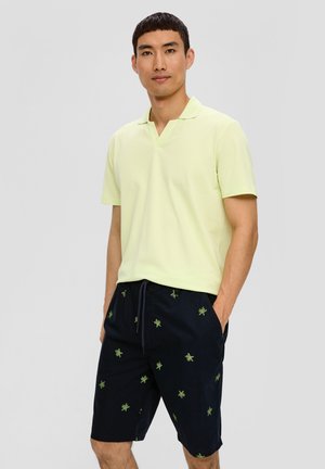 Polo vert clair avec un col en V et des manches courtes, associé à un short bleu marine orné de broderies de feuilles vertes et d'une ceinture à cordon.