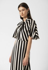 Black and white striped dress featuring a knotted collar, short flutter sleeves, and a flowing silhouette. Smooth fabric with a lightweight texture.