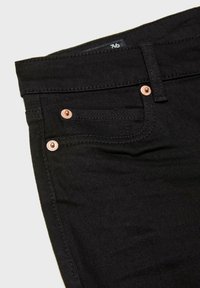 Gros plan d'un jean en denim noir montrant la poche avant, la petite poche à monnaie, la passants de ceinture et l'étiquette de taille indiquant 36.