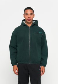 Green zip-up hooded jacket with a light gray fleece lining. Features elastic cuffs and hem, side pockets, and a small logo on the chest.