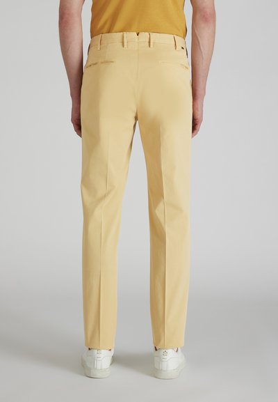 Żółte chinosy o standardowym kroju, z paskami na pasek i tylnymi kieszeniami. W zestawie z białymi sneakersami. Gładka tekstura i dopasowany fason.
