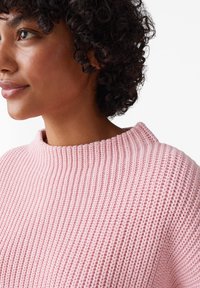 Maglione a maglia di un rosa chiaro con un design texture a coste e un collo rotondo alto, che mette in mostra un tessuto morbido in una vista ravvicinata.