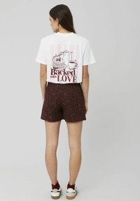 T-shirt blanc à manches courtes avec un design graphique représentant une théière, une tasse et des crêpes, le texte indique « Préparé avec AMOUR ». Associé à un short bordeaux.